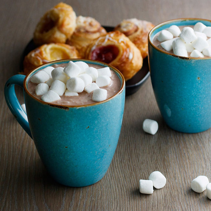 Two mugs of hot chocolate topped with marshmallows, next to a plate of pastries.