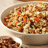 A white bowl filled with a rice and wild rice salad with pecans, red bell peppers, and red onion.