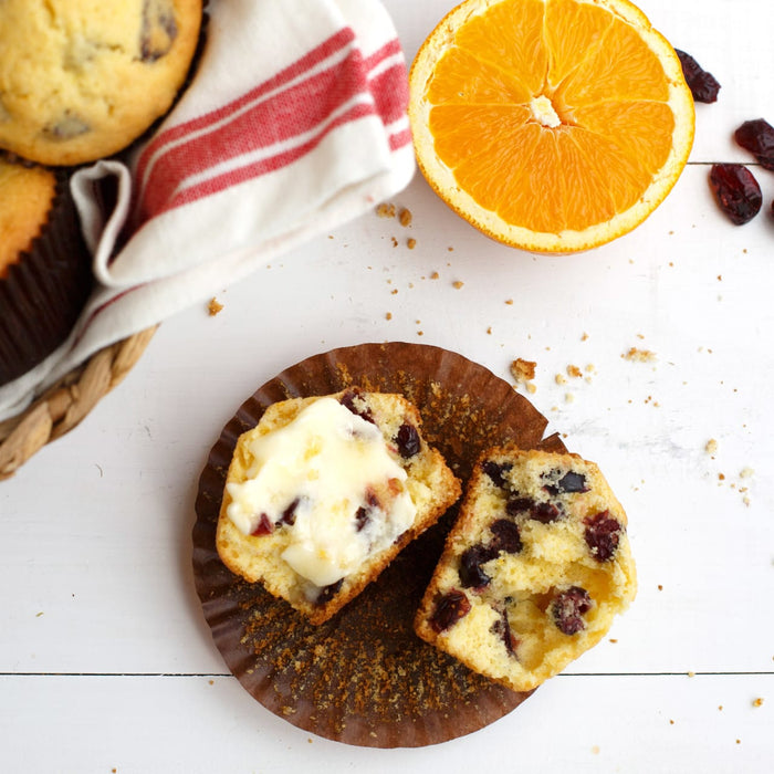 Two halves of a cranberry muffin with butter on top, next to a slice of orange and a red and white striped napkin.