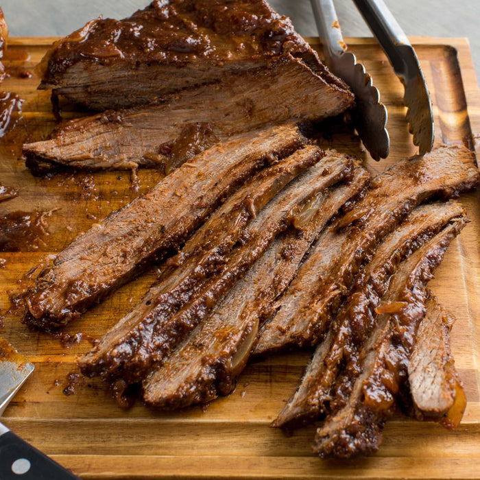 A wooden cutting board with sliced brisket and a pair of tongs.