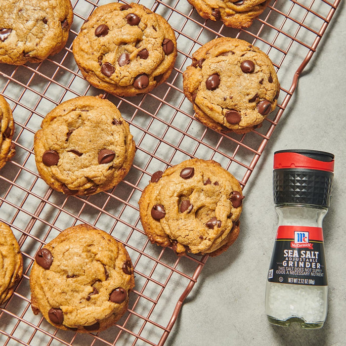 A close-up of a McCormick Sea Salt Grinder next to a cooling rack of chocolate chip cookies.