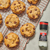 A close-up of a McCormick Sea Salt Grinder next to a cooling rack of chocolate chip cookies.