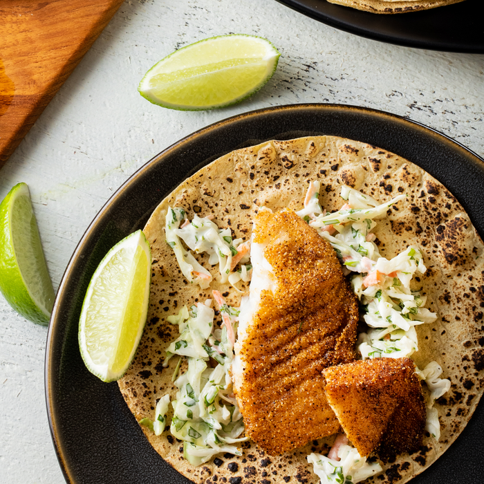 A close-up of a fish taco with slaw and lime wedges on a black plate.