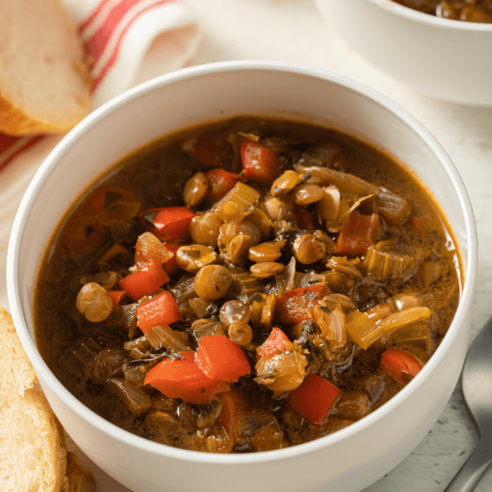 A bowl of lentil soup with red peppers and onions.