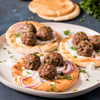 Three pita breads topped with meatball, red onion, tzatziki sauce and parsley.