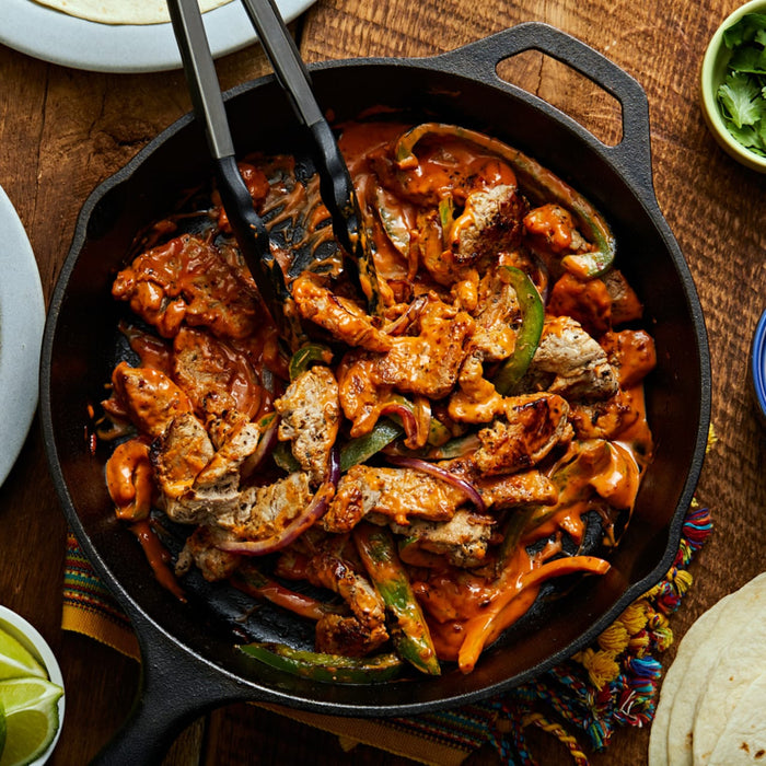 A cast iron skillet filled with chicken, peppers, onions, and a creamy sauce.