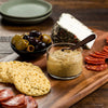 A wooden board with a variety of snacks, including olives, cheese, crackers, and mustard.