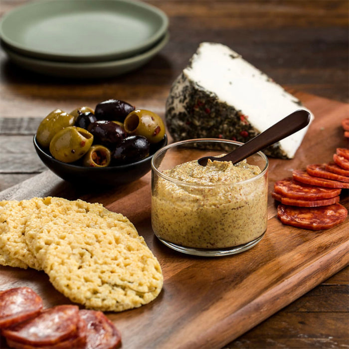 A wooden board with a variety of snacks, including olives, cheese, crackers, and mustard.