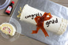 A graduation cake decorated as a diploma with a McCormick Pure Lemon Extract bottle nearby.