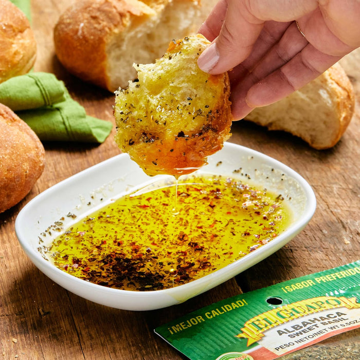 A hand dips a piece of bread into a bowl of El Guapo Albahaca Sweet Basil.