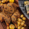A close-up of a roasted chicken with potatoes and lemons, seasoned with McCormick Grill Mates Garlic &amp; Crushed Herb seasoning.