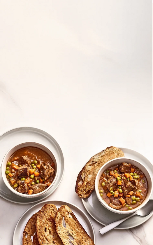 Two bowls of beef stew with bread on a white background