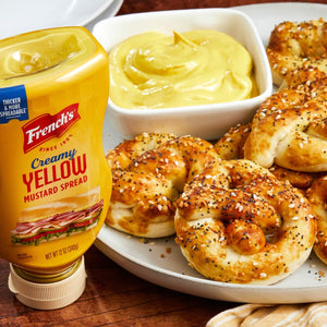 A bottle of Frenchs Creamy Yellow Mustard next to a plate of pretzel bites with a small bowl of mustard.