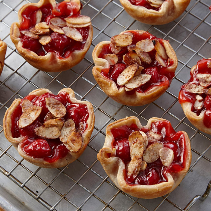 Cherry hand pies with almond slices on top are arranged on a wire rack.