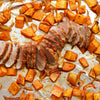 A close-up of a baking sheet with roasted sweet potatoes, onions, and pork tenderloin.