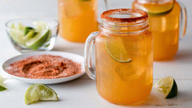 Mason jar with Mexican-style margarita, lime wedges, and salt on a white surface.