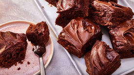 Chocolate brownies with a fork on a plate and more brownies on a tray.