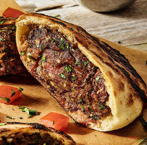 A close up view of a grilled pita bread pocket stuffed with a seasoned meat filling and fresh herbs as part of a recipe for .