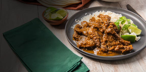 Plated dish of meat with sauce and rice on a wooden table with a green napkin.