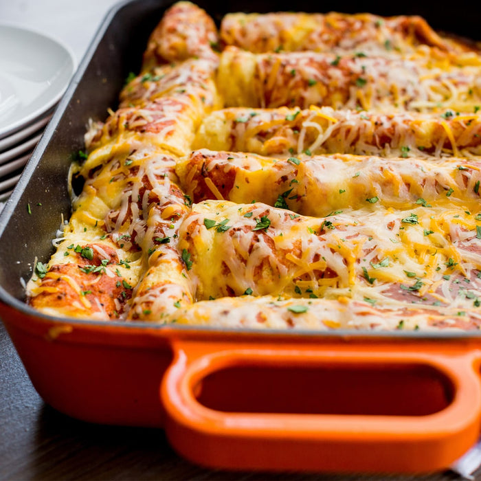 A close-up of a casserole dish filled with cheesy enchiladas.