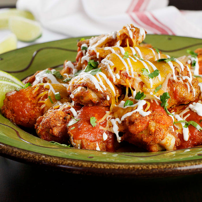 A plate of chicken wings covered in cheese, sour cream, and cilantro.