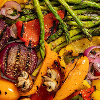 Grilled vegetables including asparagus, red onions, and bell peppers on a baking sheet.