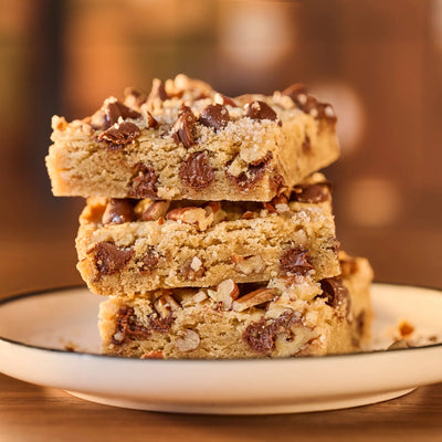 Stack of chocolate chip cookie bars on a white plate with a blurred background