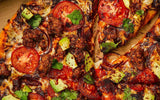 Close-up of a pizza with tomatoes, onions, and cilantro on a wooden surface