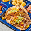Two carnitas tacos filled with rice, shredded pork, lettuce, and charred corn are served on a blue tray alongside fresh pineapple and pico de gallo.