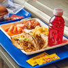 A school lunch tray features two street tacos filled with meat and corn salsa alongside baby carrots, pineapple chunks, pico de gallo, a red sports drink, and two packets of Cholula Hot Sauce.