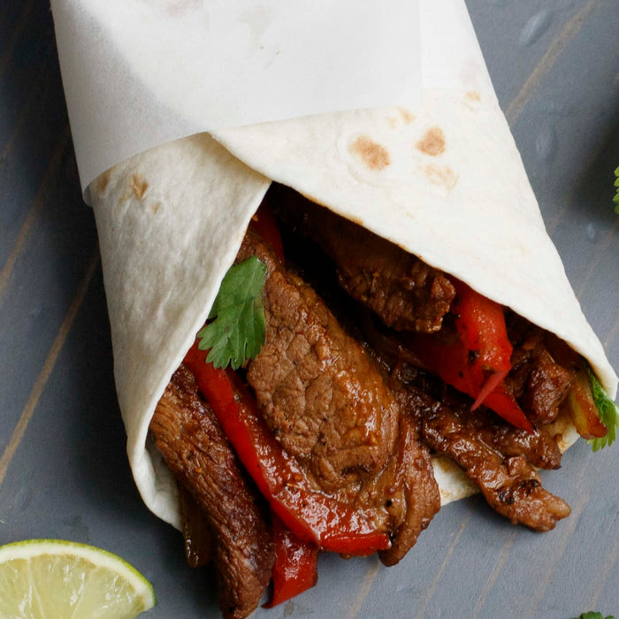 A close-up of a burrito filled with steak, peppers, and cilantro.