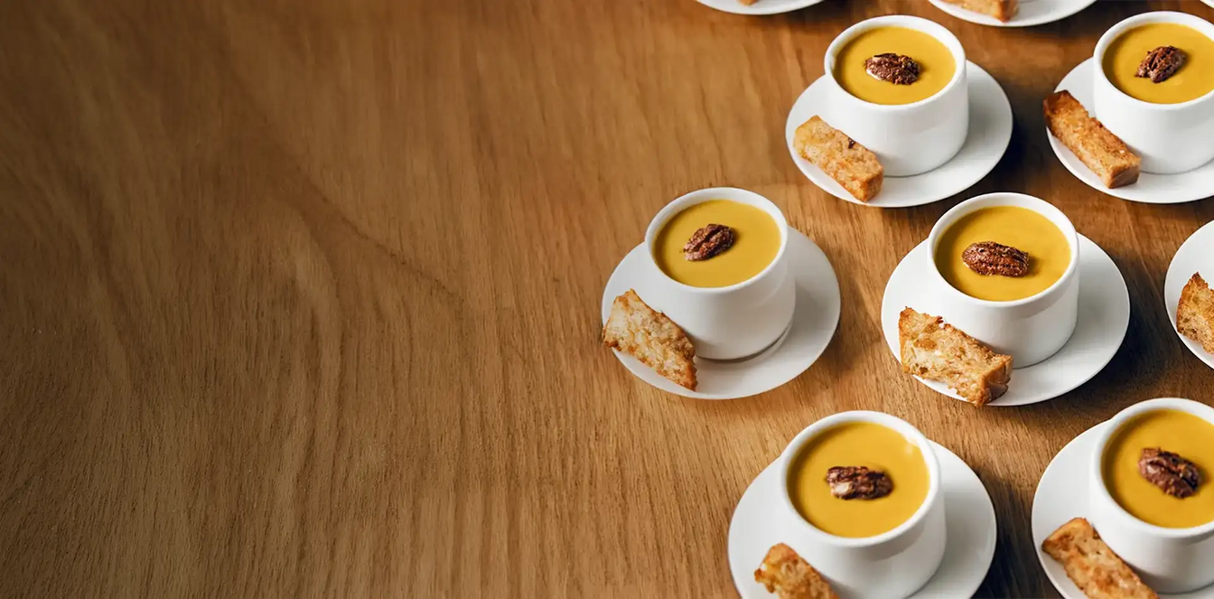 Multiple small white cups filled with a yellow dessert on a wooden table.