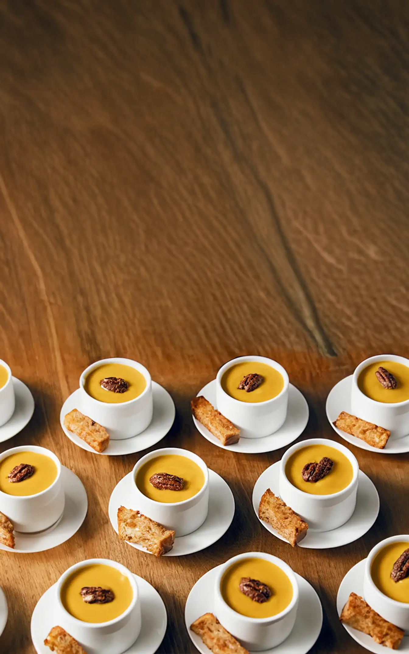 Multiple small white cups filled with a yellow dessert on a wooden table.