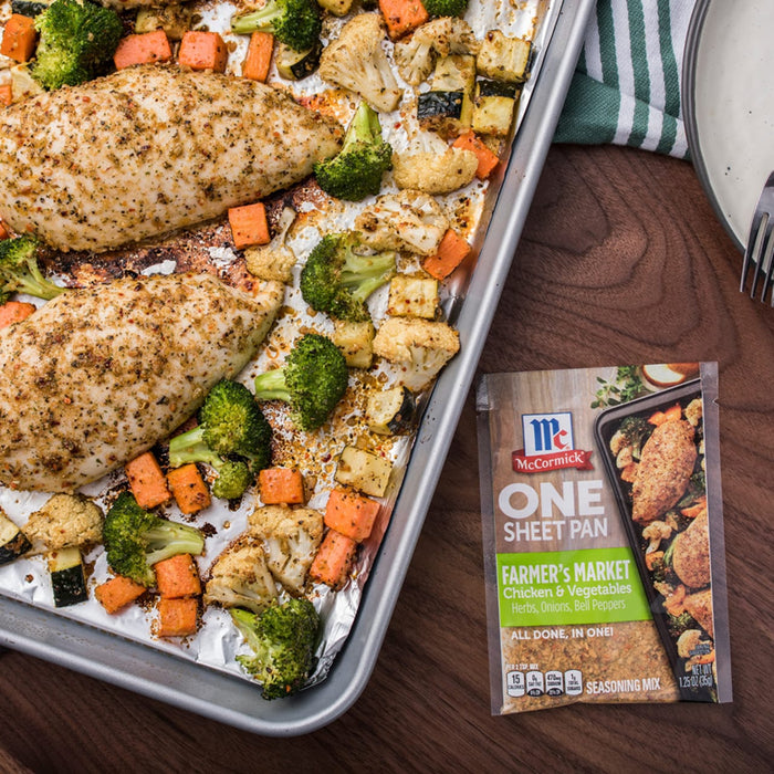 A McCormick One Sheet Pan Farmers Market seasoning packet next to a baking sheet with chicken and vegetables.