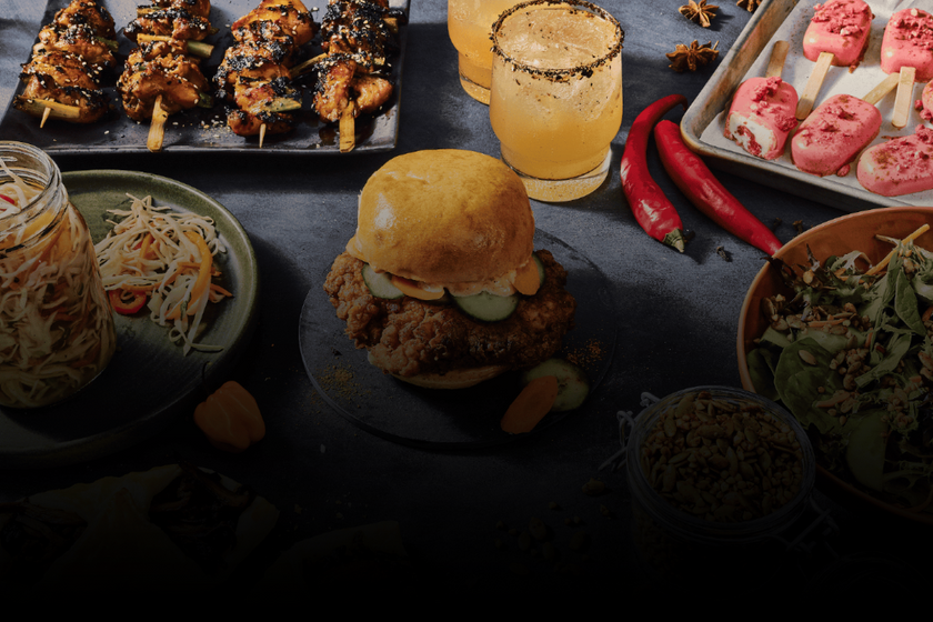 Assorted food items including a burger, skewers, and bowls on a dark surface