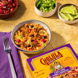 A bowl of Cholula Chili Lime Pork Carnitas Burrito Bowl with a fork and other ingredients on the side.