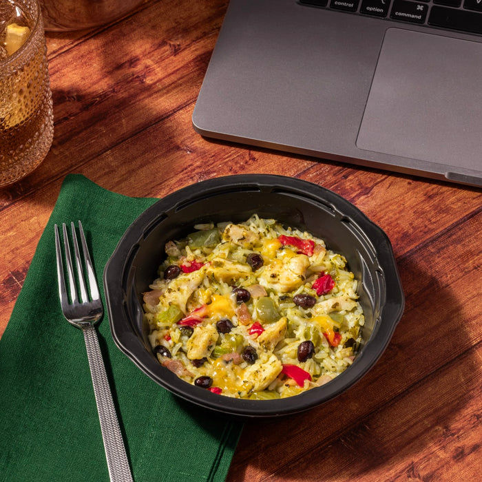 A black bowl of chicken and rice with black beans, peppers, and cheese sits on a green napkin next to a fork.