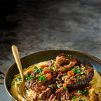 Slow-braised beef osso buco served over creamy polenta, garnished with fresh herbs.