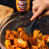A hand is tossing cauliflower florets in a bowl with Franks RedHot Wings sauce.