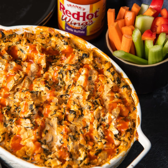 A white casserole dish filled with a creamy spinach and chicken dip topped with Franks RedHot Buffalo Wing Sauce.