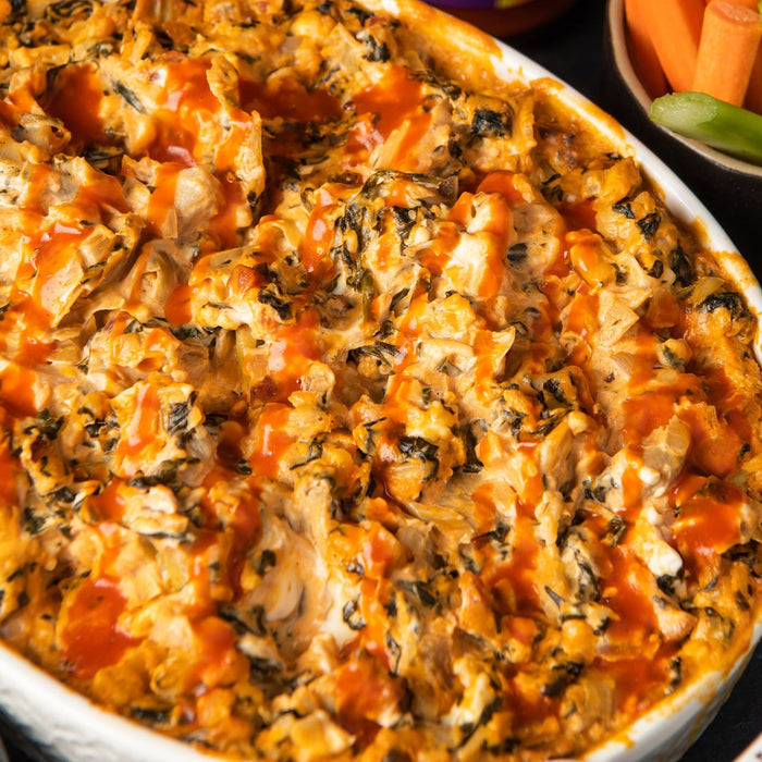 A white casserole dish filled with a creamy spinach and chicken dip topped with Frank's RedHot Buffalo Wing Sauce.