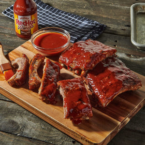 A wooden cutting board with Franks RedHot Wings BBQ sauce and ribs.
