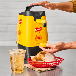 A hand pours Frenchs Classic Yellow Mustard into a small container.