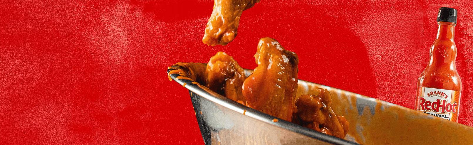 Baked wings with a bottle of Frank's RedHot sauce on a red background