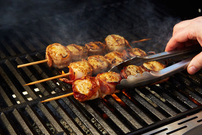 Skewers of food being grilled on a barbecue with tongs