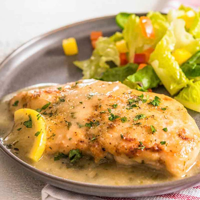 A plate of chicken breast with a lemon sauce and a side salad.