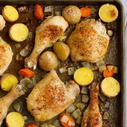 A close-up of a baking sheet with roasted chicken, potatoes, carrots, and onions.