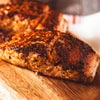 A close up of a piece of salmon cooked to perfection on a wooden cutting board.