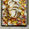 A close-up of a baking sheet with roasted pork tenderloin, potatoes, and red peppers.