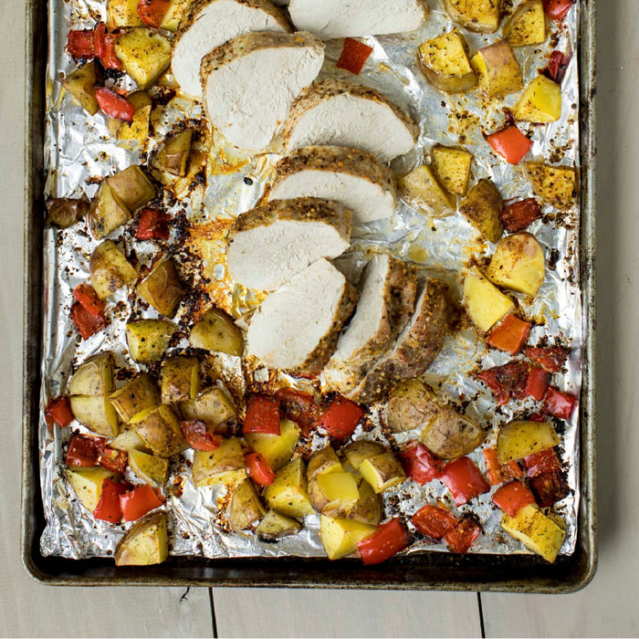 A close-up of a baking sheet with roasted pork tenderloin, potatoes, and red peppers.